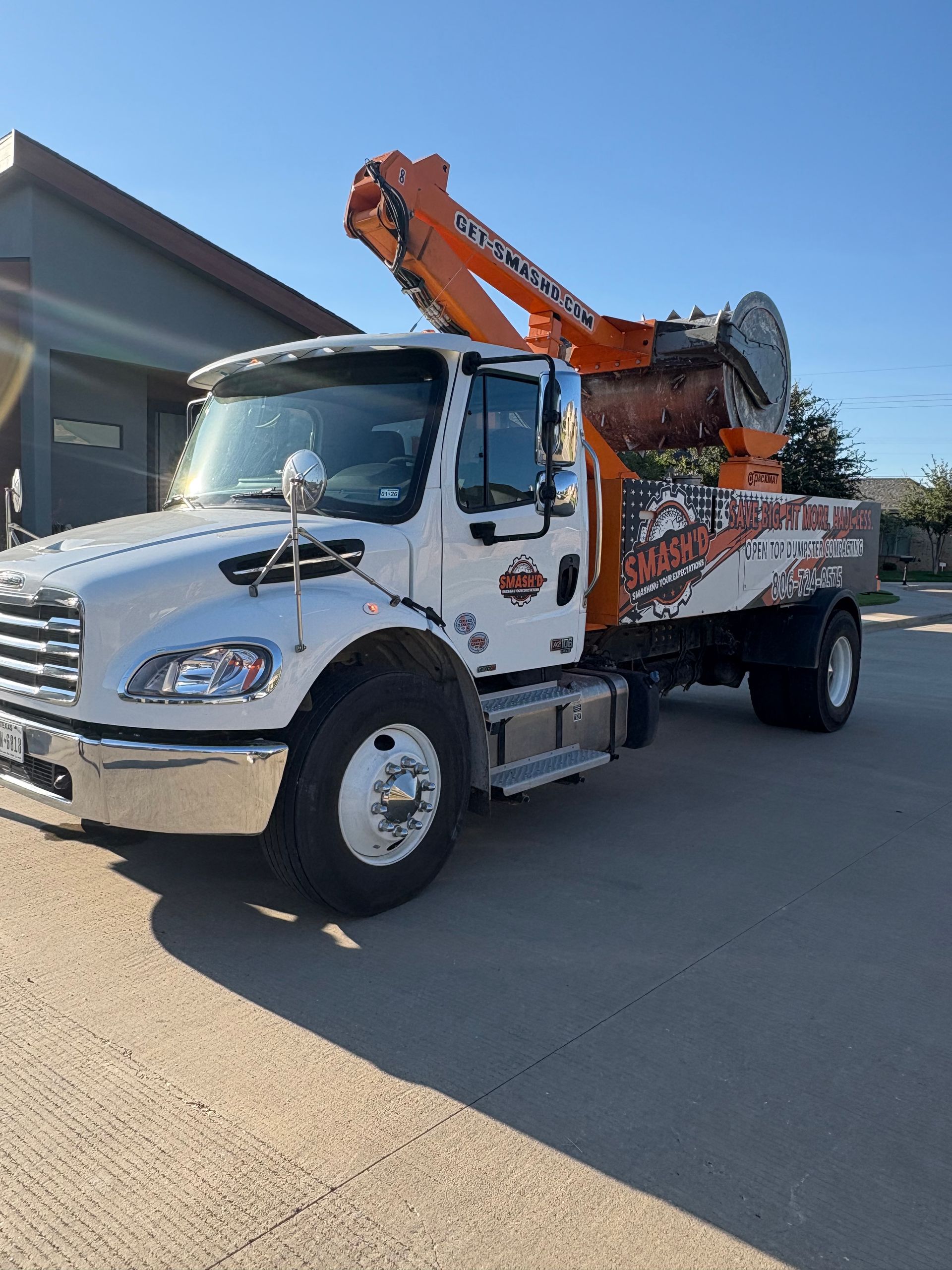 A white utility truck with an orange boom crane parked on a paved lot under a clear blue sky.