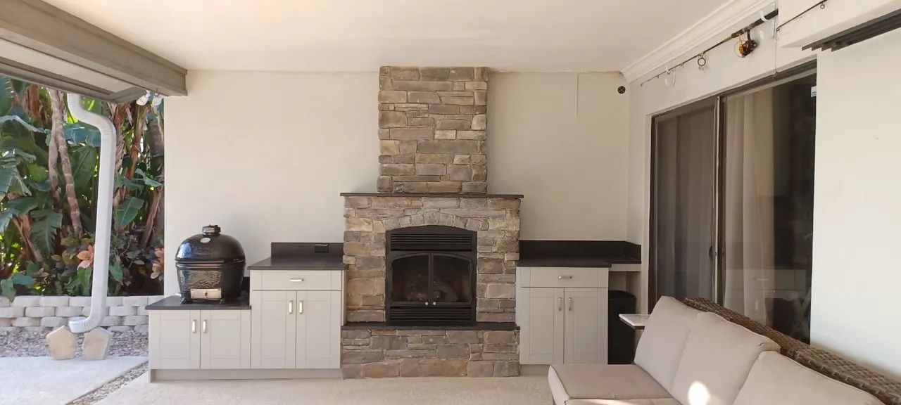 Outdoor patio with a stone fireplace, cabinets, a grill, and a couch.