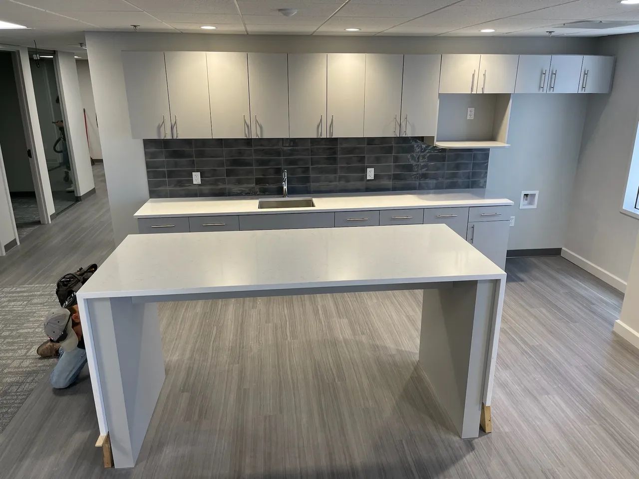 Office kitchen with white cabinets, grey backsplash, and a white island.