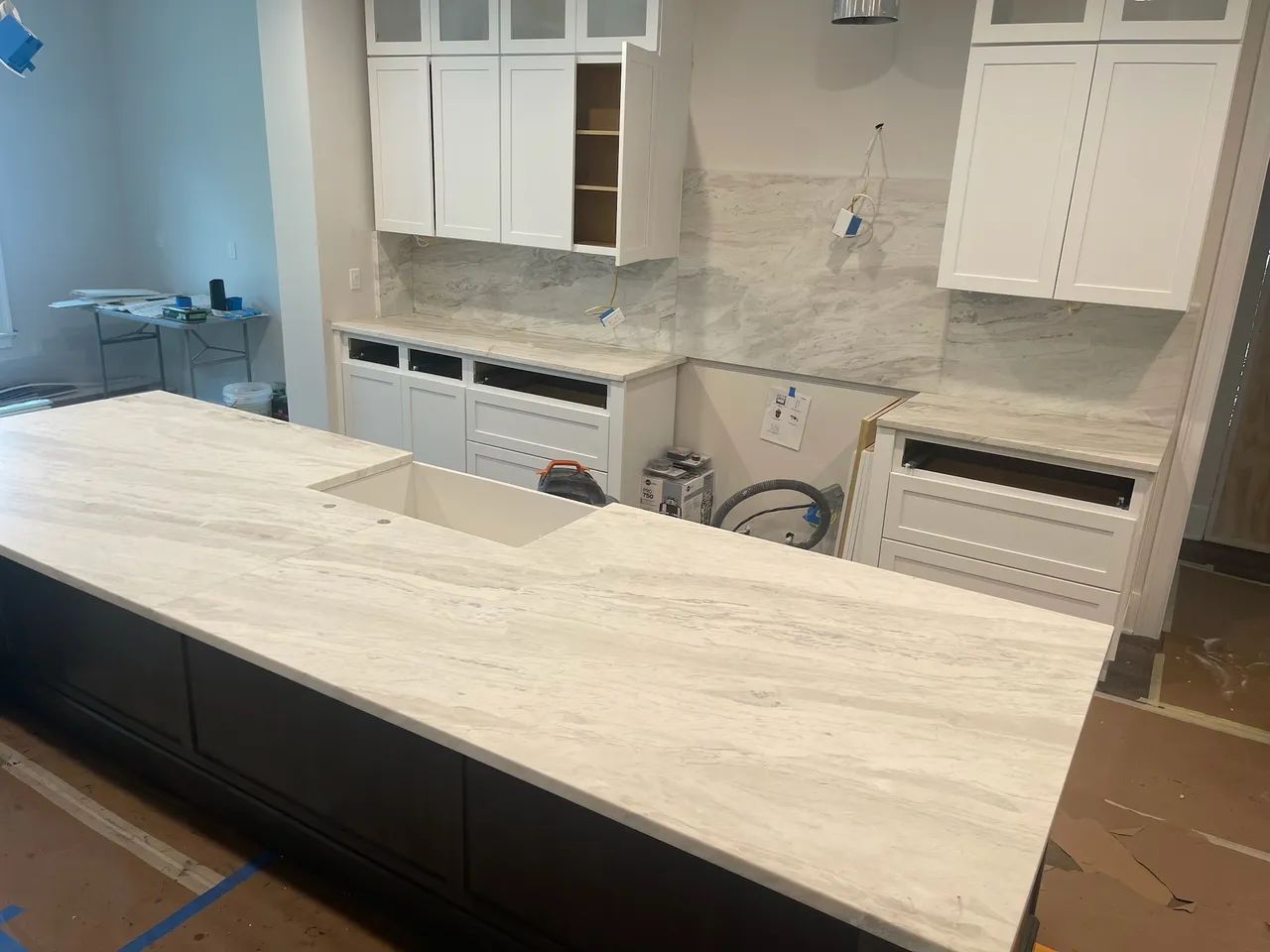 Kitchen renovation: white countertops installed on dark island and white cabinets, backsplash and countertop installed along the wall.