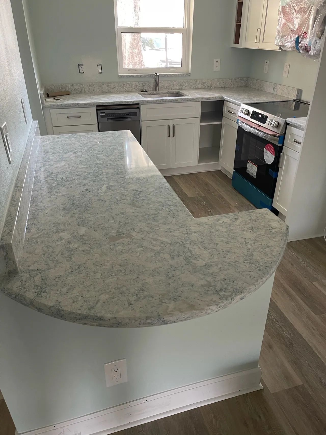 U-shaped kitchen with light blue walls, white cabinets, and gray countertops. Stainless steel appliances and a peninsula.
