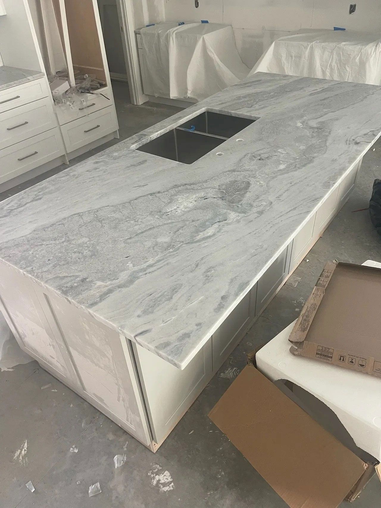 Kitchen island with a gray and white marbled countertop and built-in sink. Cabinets below.