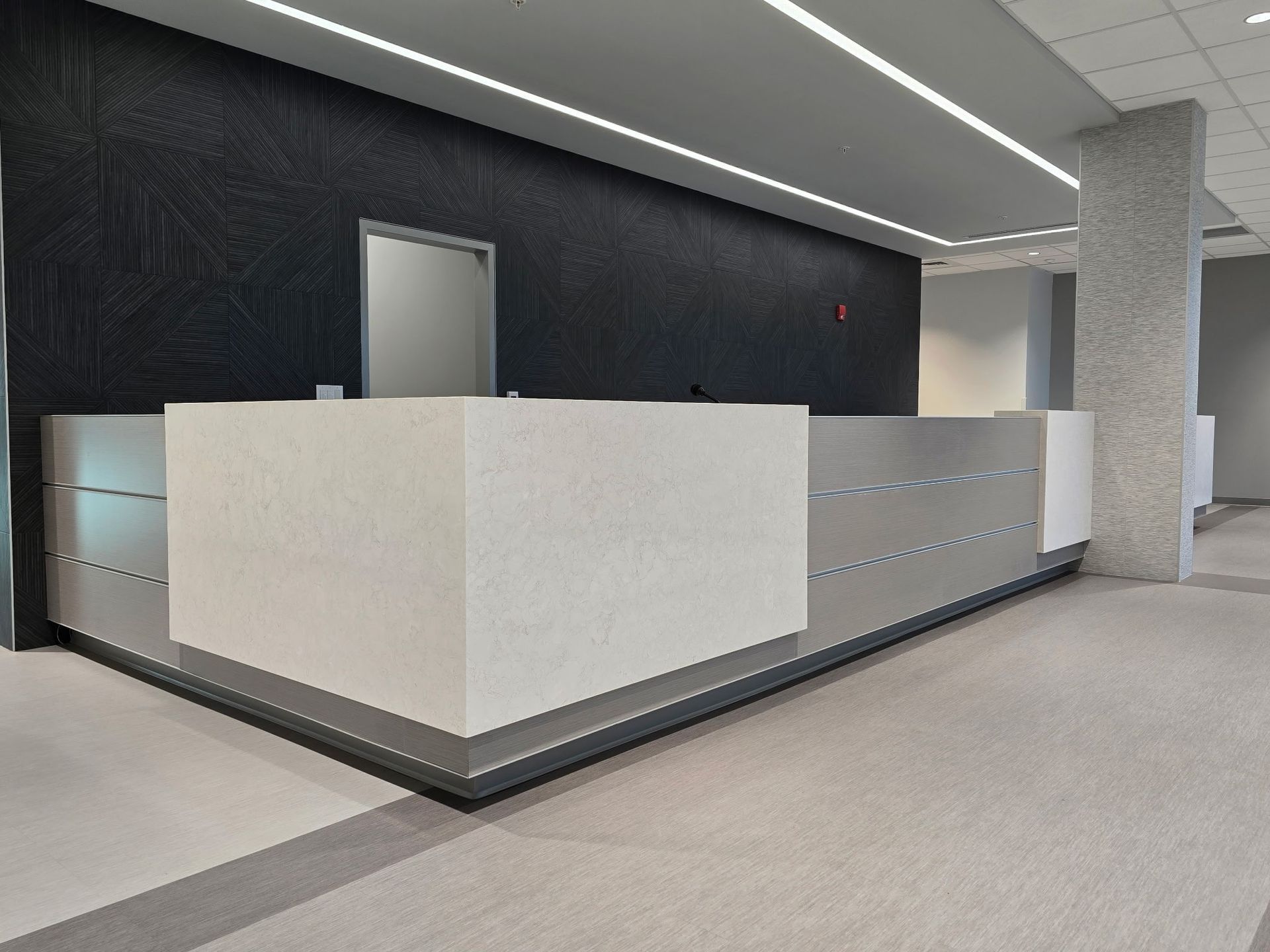 Modern office reception desk with white and silver panels, against a textured black wall.