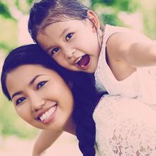 A little girl is sitting on a woman 's back and smiling