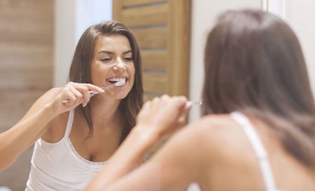 A woman is brushing her teeth in front of a bathroom mirror.