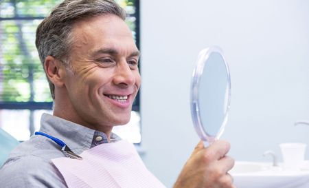 A man is smiling while looking at his teeth in a mirror.