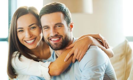 A man and a woman are hugging each other while sitting on a couch.