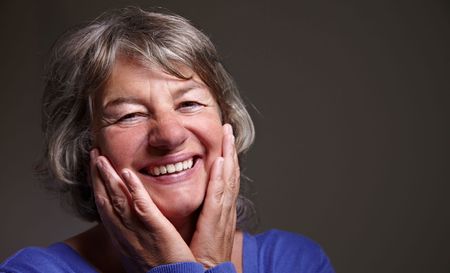 An older woman is smiling with her hands on her face.