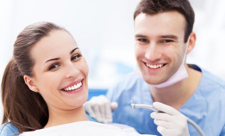 A woman is smiling while sitting in a dental chair next to a dentist.