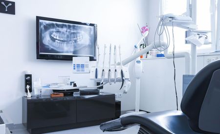 A dental office with a dental chair and a television on the wall.