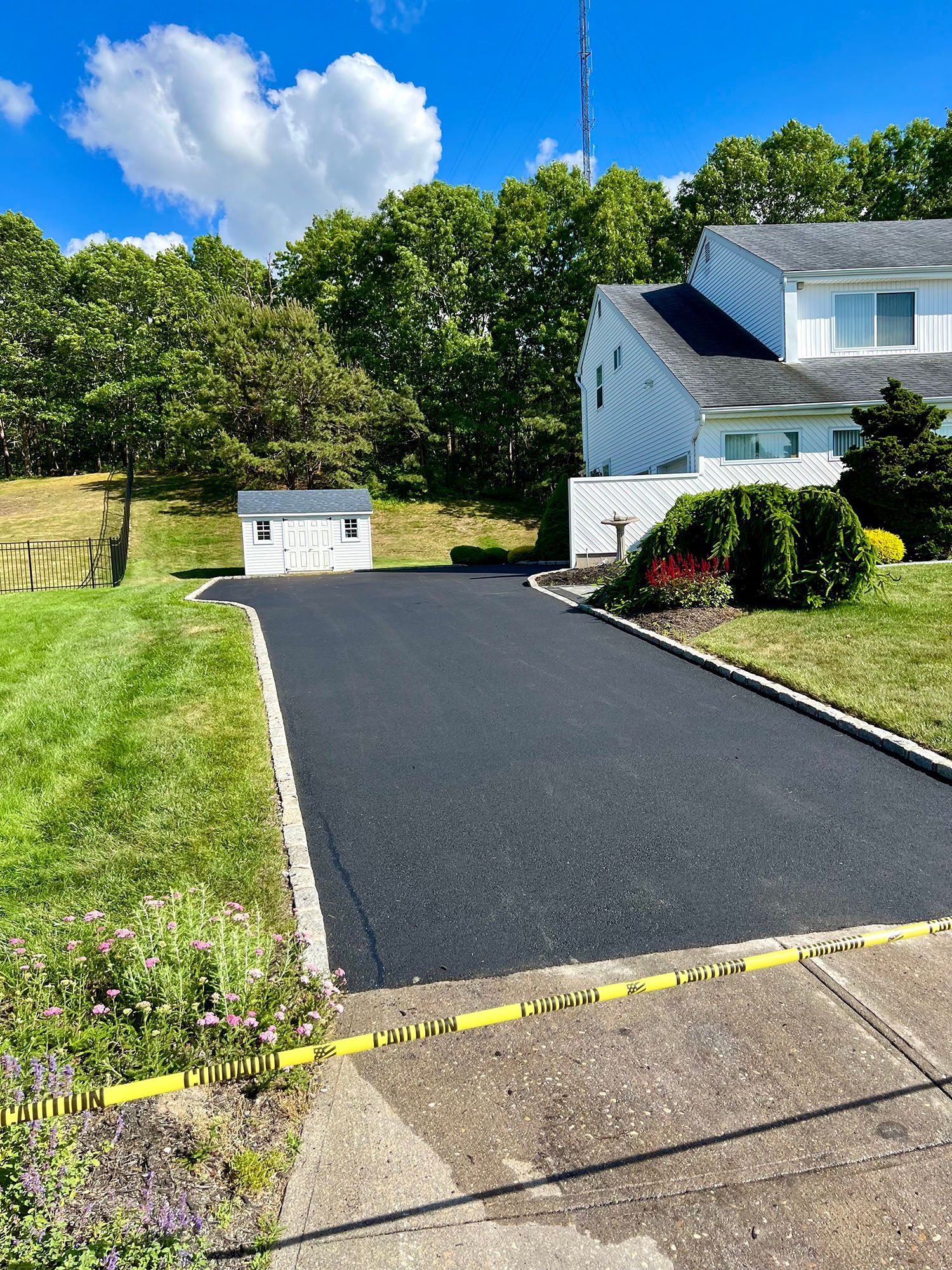 A black driveway leading to a white house surrounded by grass and trees.