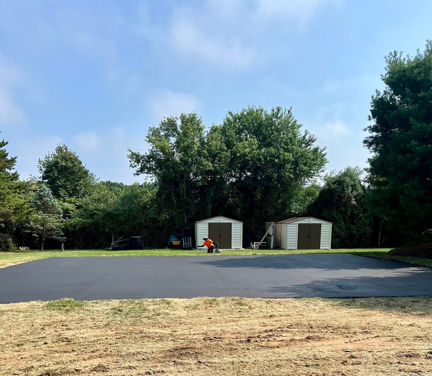 A parking lot with two sheds and trees in the background.