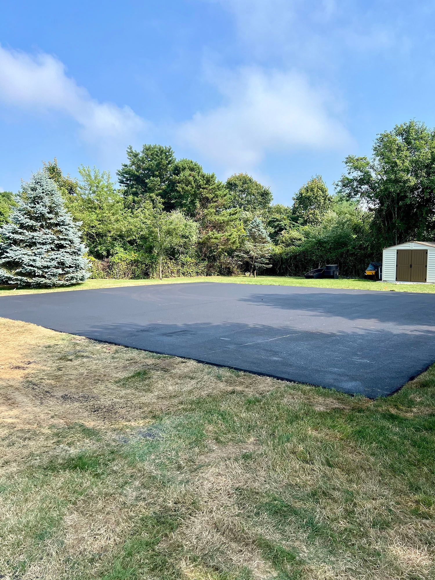 There is a large asphalt driveway in the middle of a grassy field.