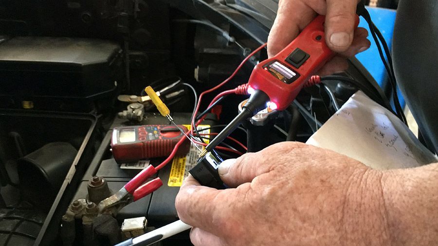 A person is working on a car battery with a multimeter.
