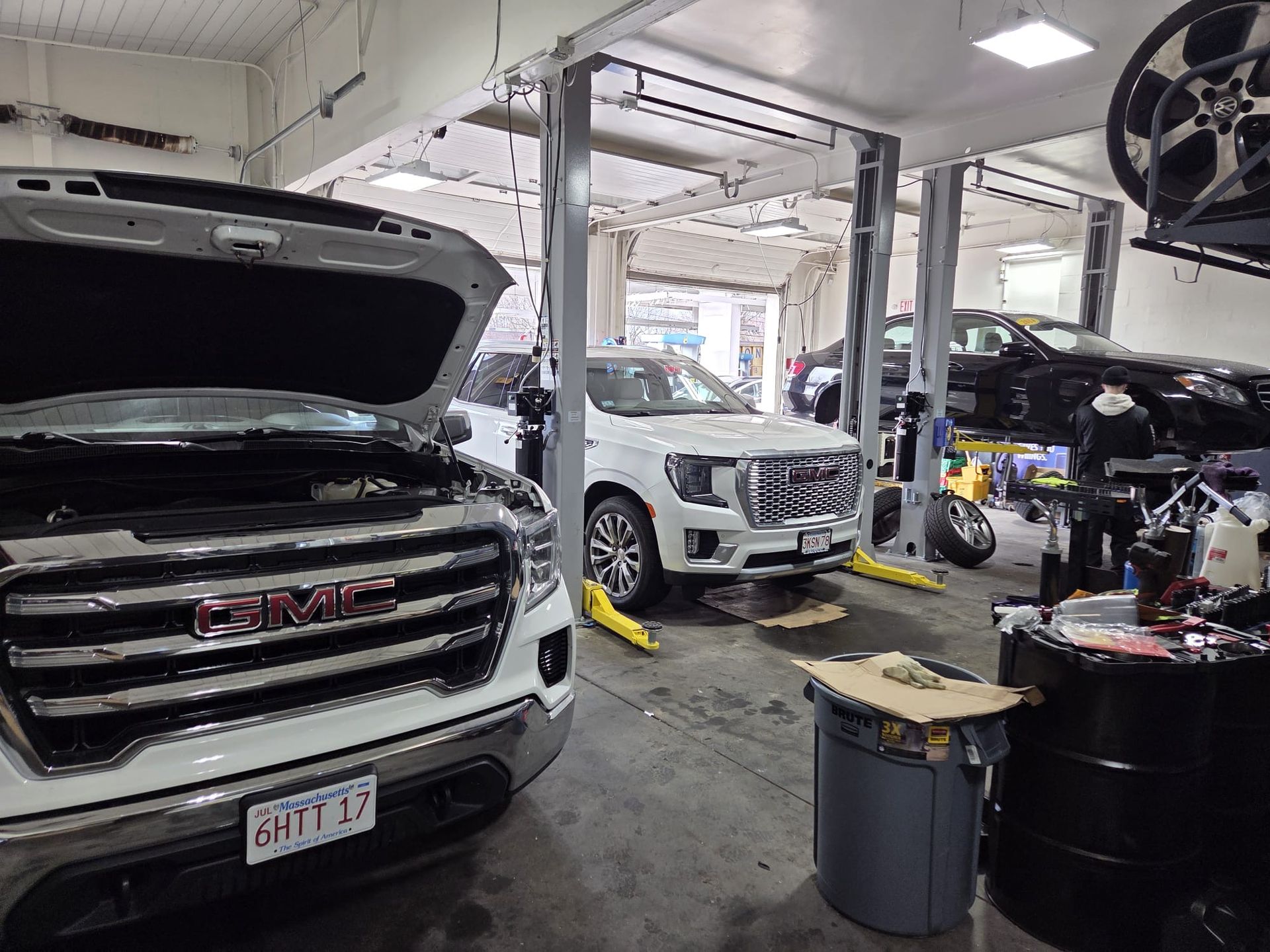 Auto repair shop with several vehicles on lifts, including a white GMC with its hood open.