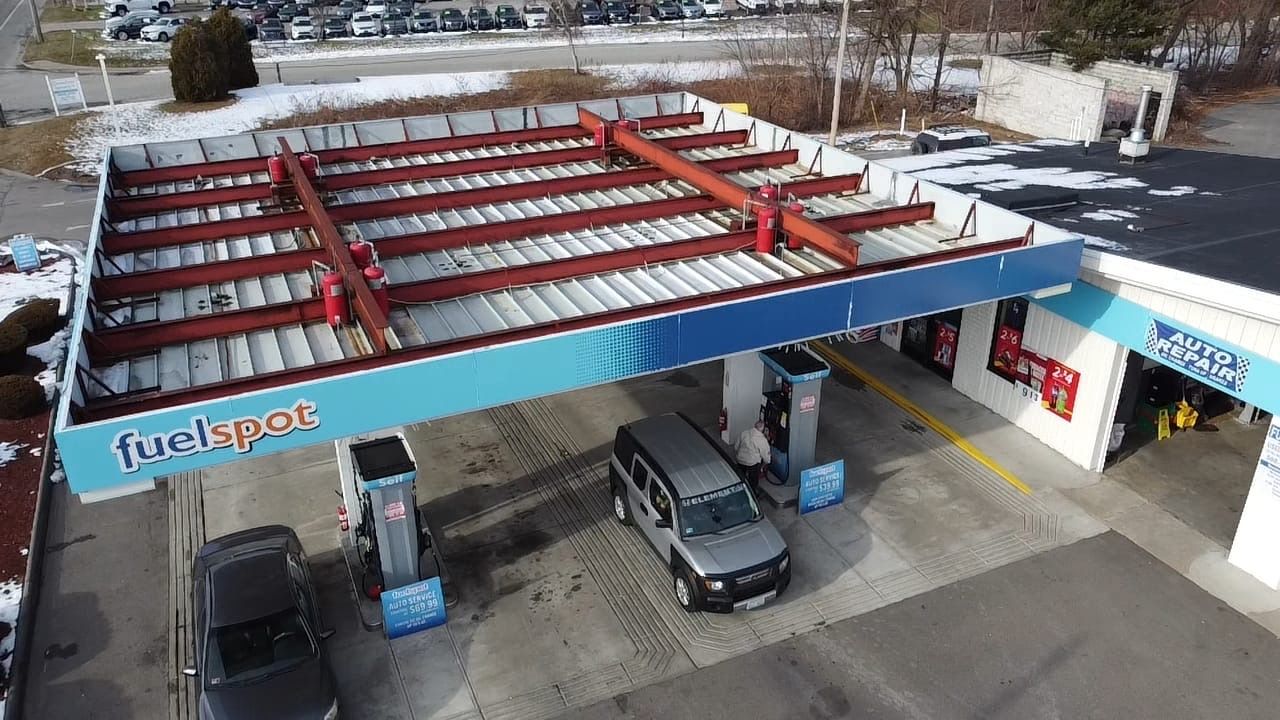 Gas station canopy with exposed red roof framing and cars at the pumps in a snowy lot
