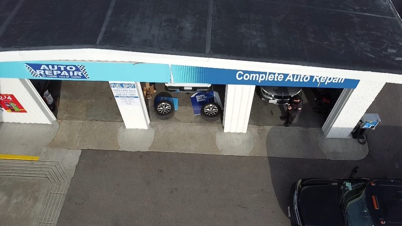 Top-down view of a car service garage with scooters parked in open bays and a black car at right.