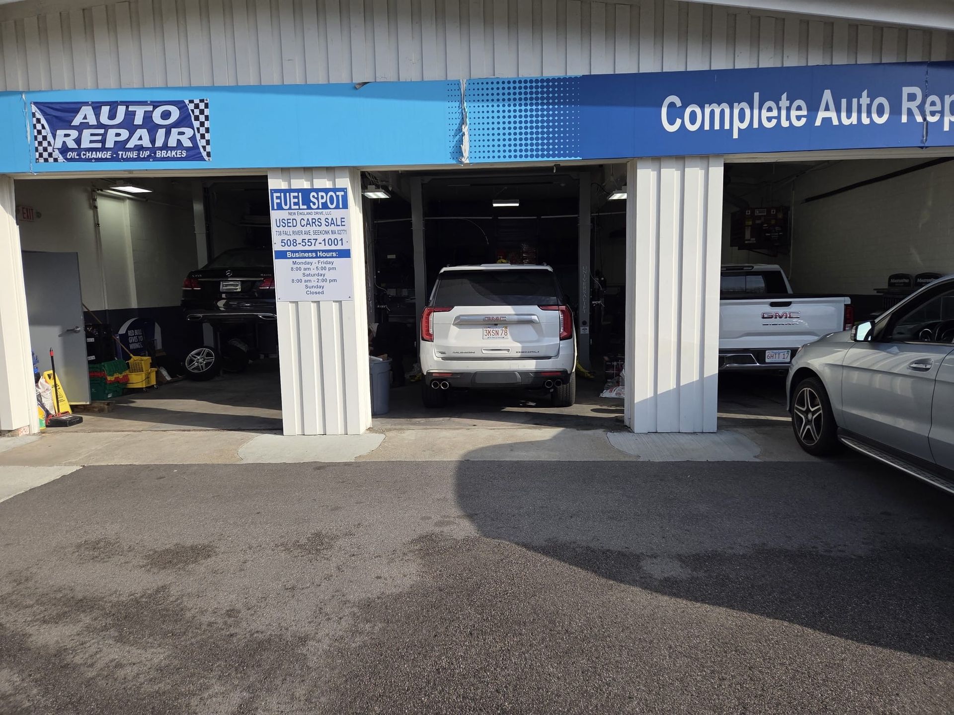 Auto repair shop bays with cars parked inside and outside, blue sign above entrance