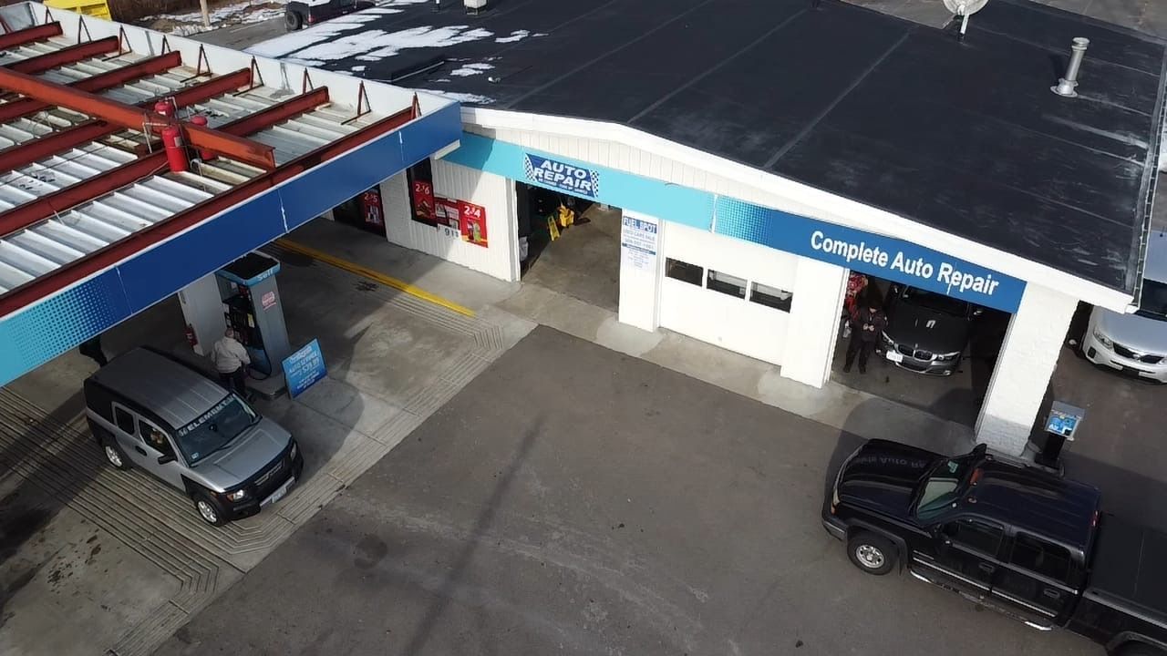 Aerial view of an auto repair shop with several parked vehicles under a blue-and-white canopy.