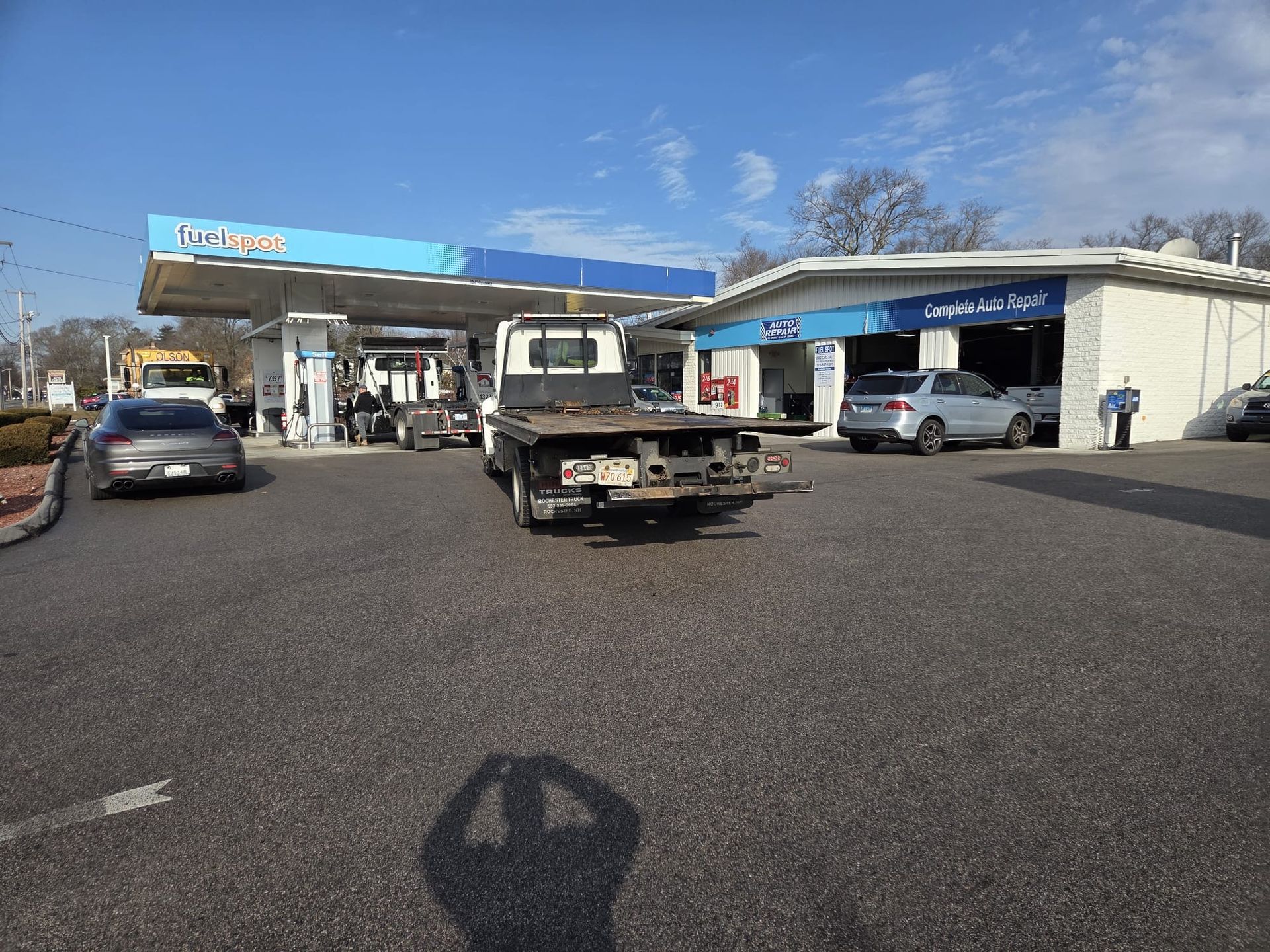 Gas station with a pickup truck at the pumps and cars parked under a blue canopy.