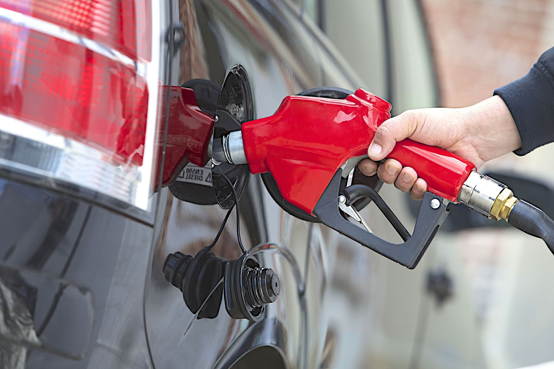 Person refueling a black car with a red gas pump nozzle at a gas station.