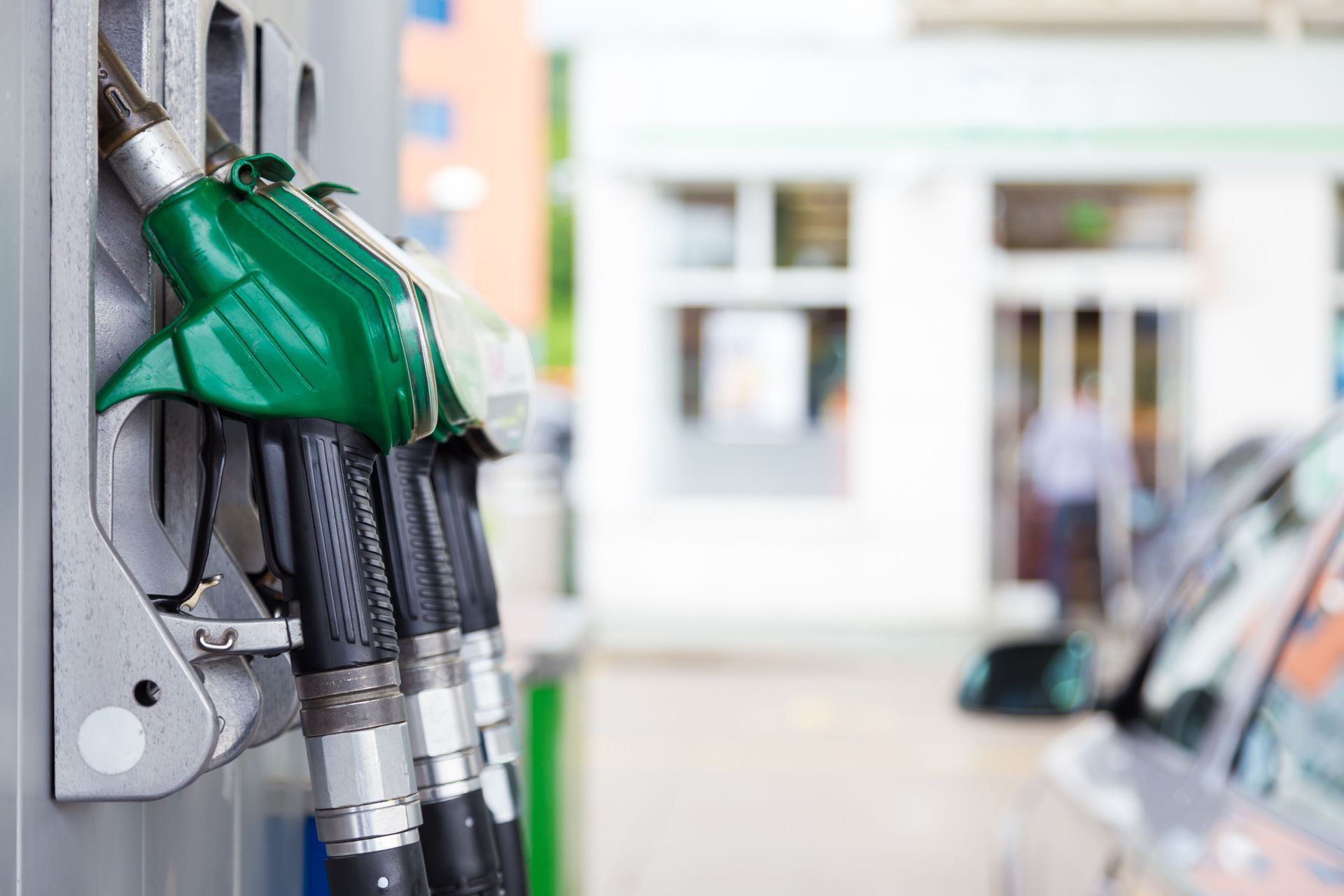 Green fuel nozzles at a gas station pump, with cars blurred in the background.