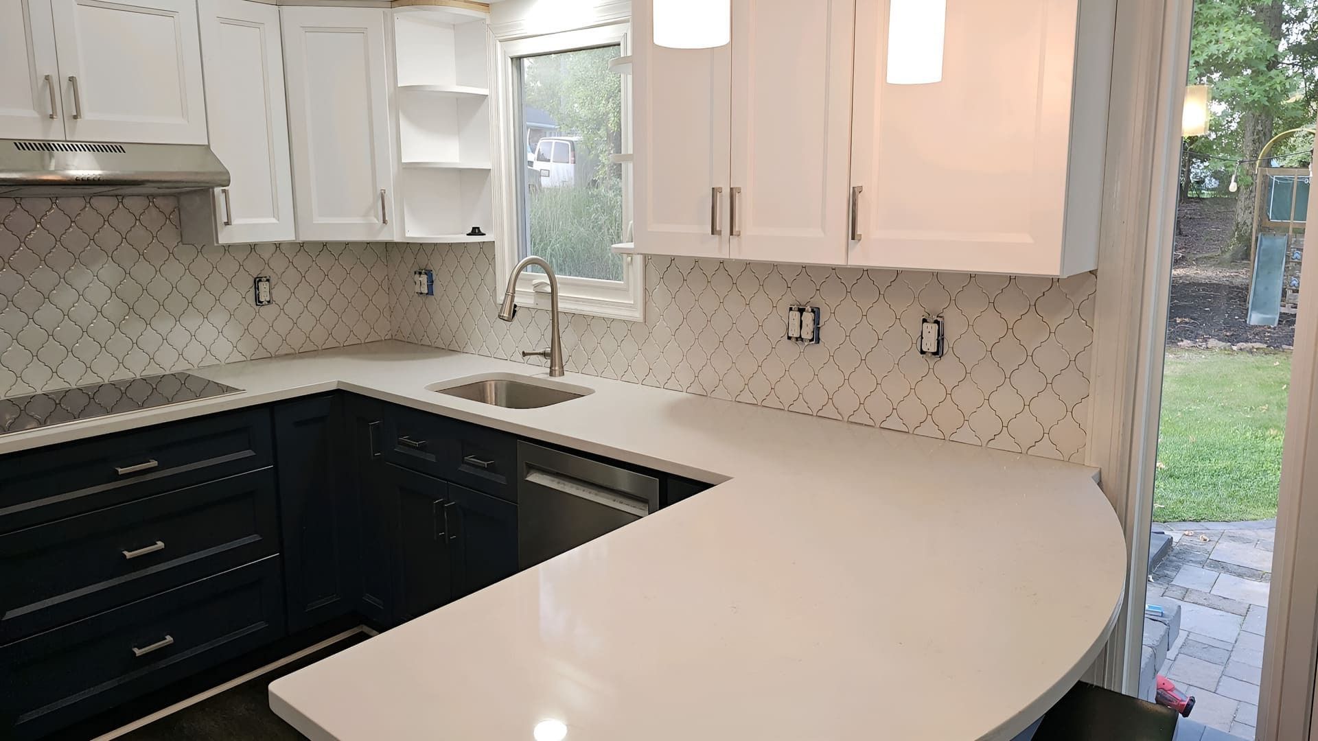 A kitchen with black cabinets , white counter tops , a sink , and a window.