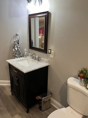 A bathroom with a sink , toilet , mirror and trash can.