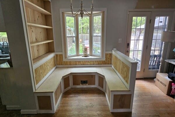 There is a bench in the middle of the room next to a window.