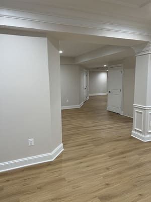 An empty basement with hardwood floors and white walls.