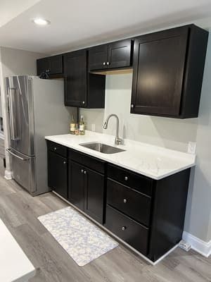 A kitchen with black cabinets , a sink , and a refrigerator.