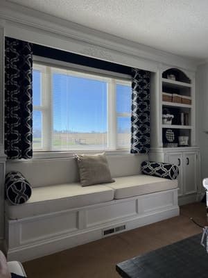 A living room with a window seat and built in shelves.