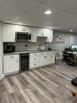 A kitchen with white cabinets , a microwave , a refrigerator , a sink , and a desk.