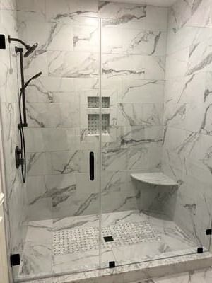 A bathroom with marble tiles and a walk in shower with a glass door.