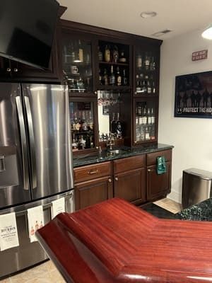 A kitchen with stainless steel appliances , wooden cabinets , a refrigerator and a bar.