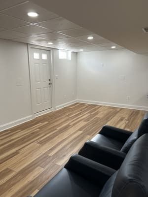A living room with hardwood floors , a couch , chairs and a door.