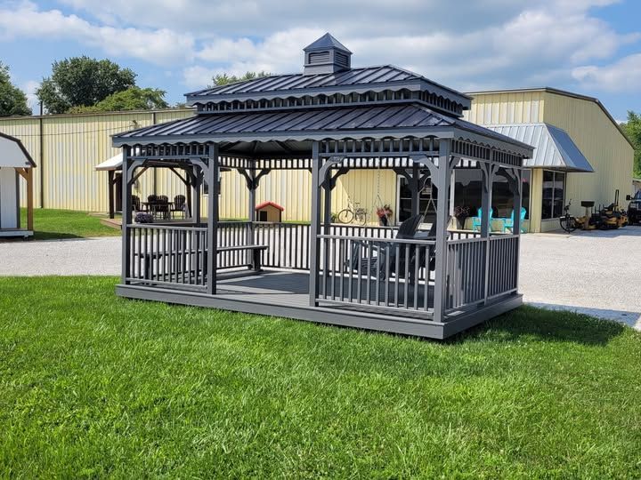 A gazebo with a table and chairs is sitting in the grass in front of a building.