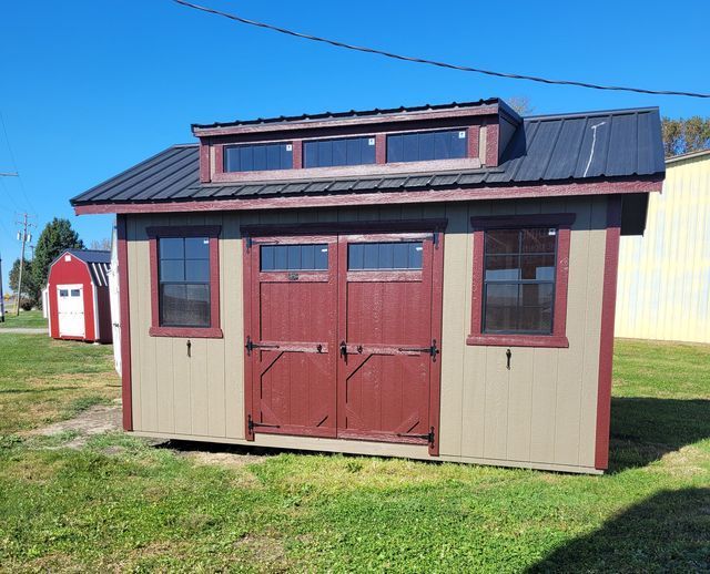 A small shed with a black roof and red doors is sitting on top of a lush green field.