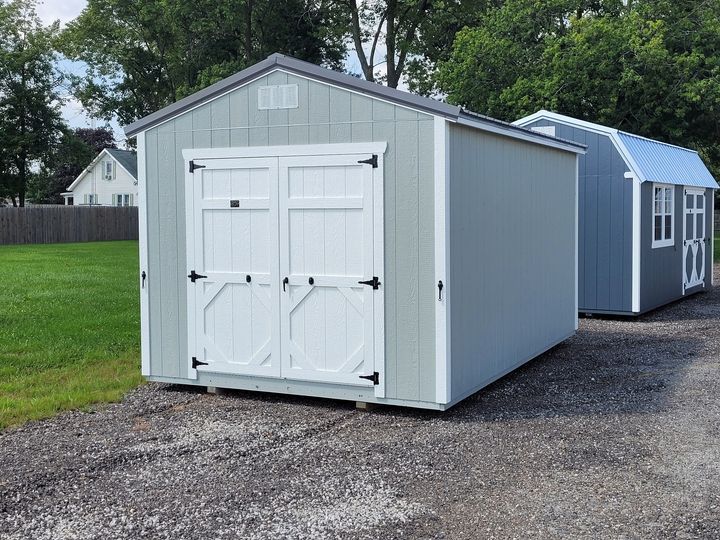Two sheds are parked next to each other on a gravel road.