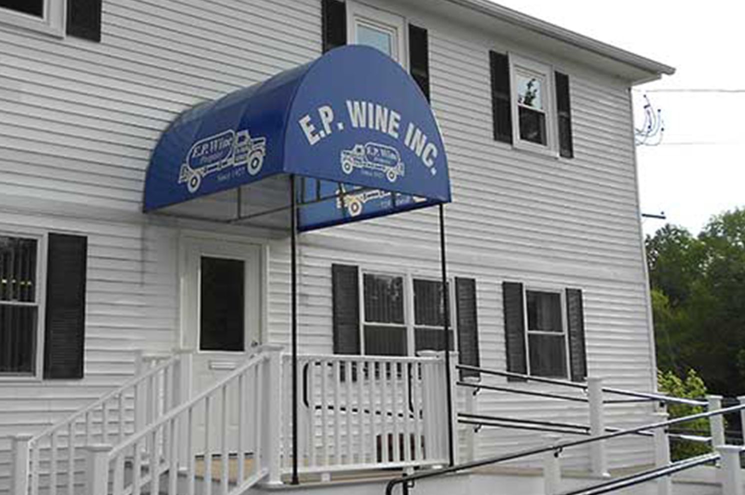 Exterior of EP Wine Inc., a white building with a blue awning over the entrance.  A wheelchair ramp is visible.