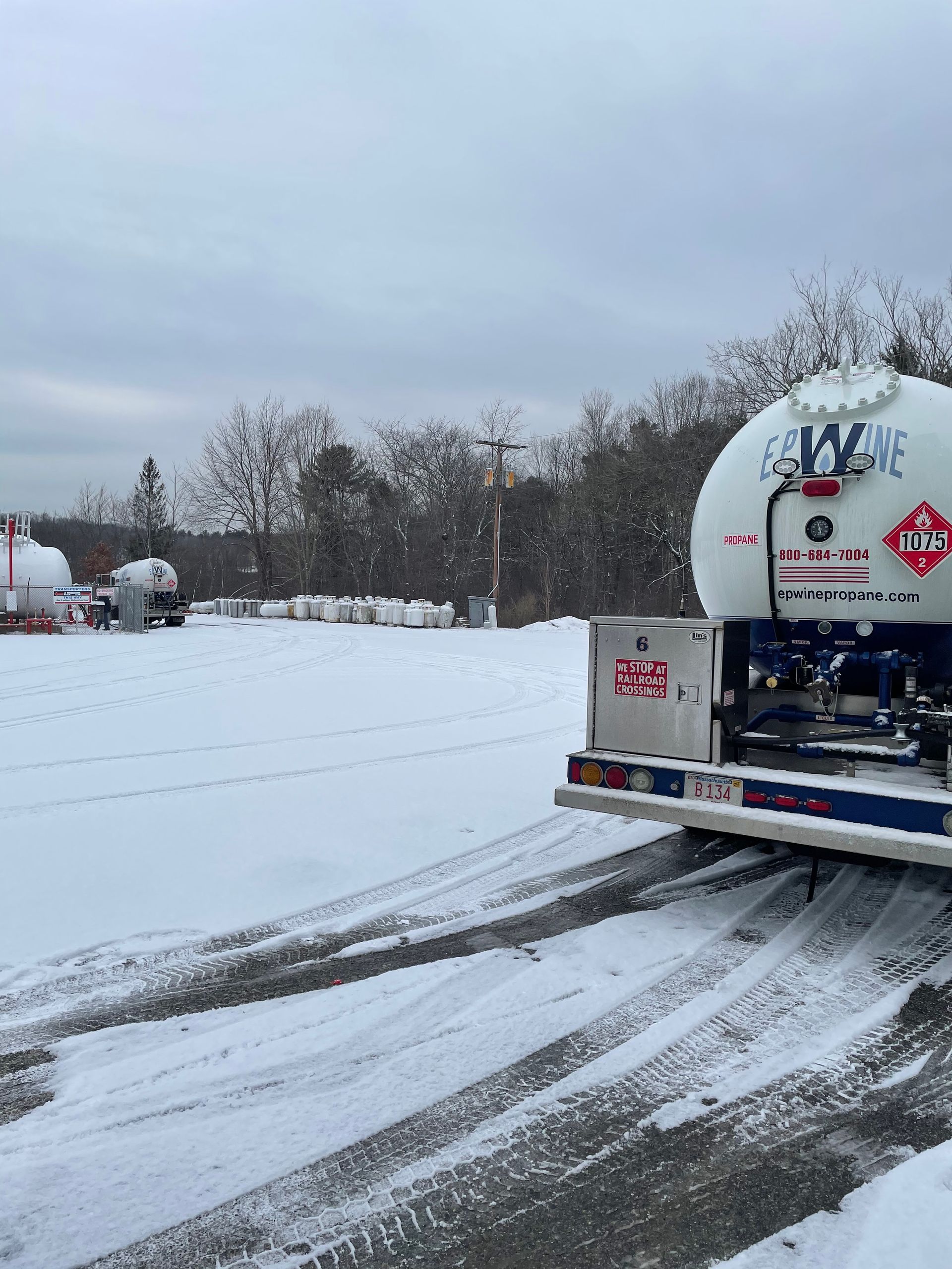 A propane tanker truck parked in a snowy lot with other tanks and overcast sky.