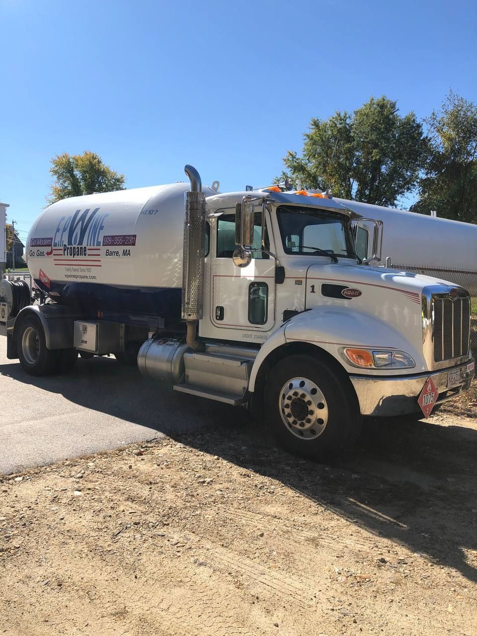 White propane tanker truck parked outdoors on dirt, sunny day.