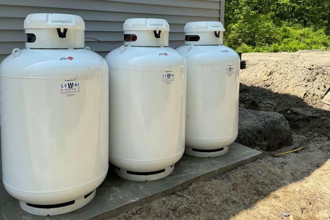 Three white propane tanks next to a building on a stone platform in an outdoor setting.