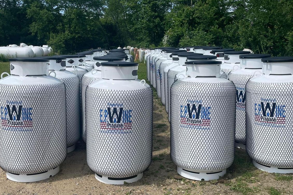 Rows of white propane tanks with black mesh coverings, outdoors.