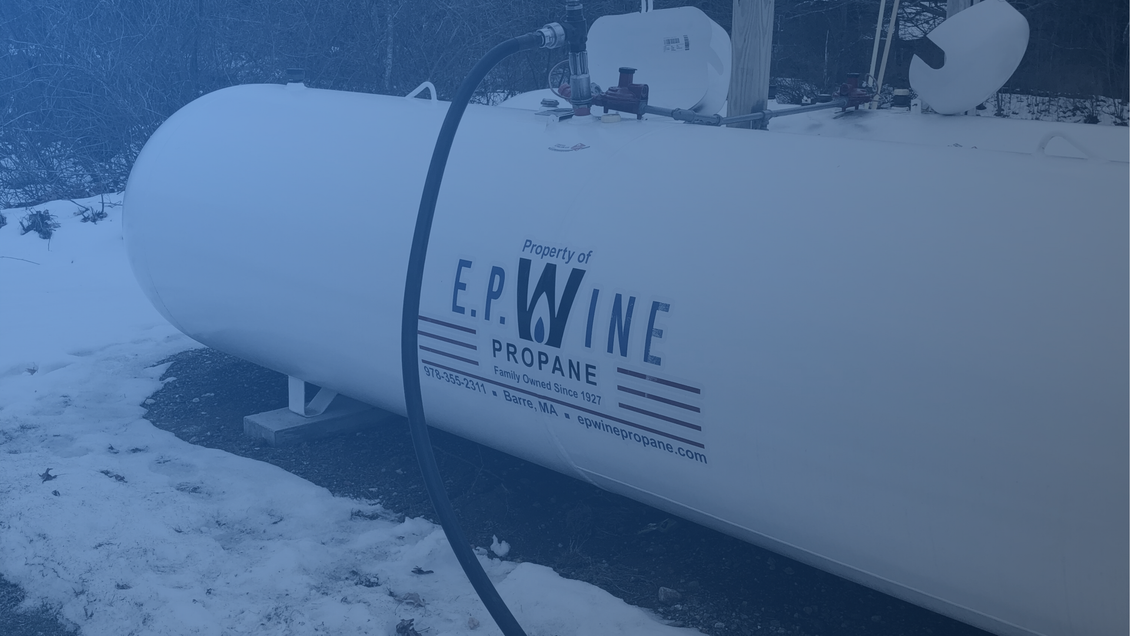 Red propane truck parked, loaded with tanks, in front of a building.