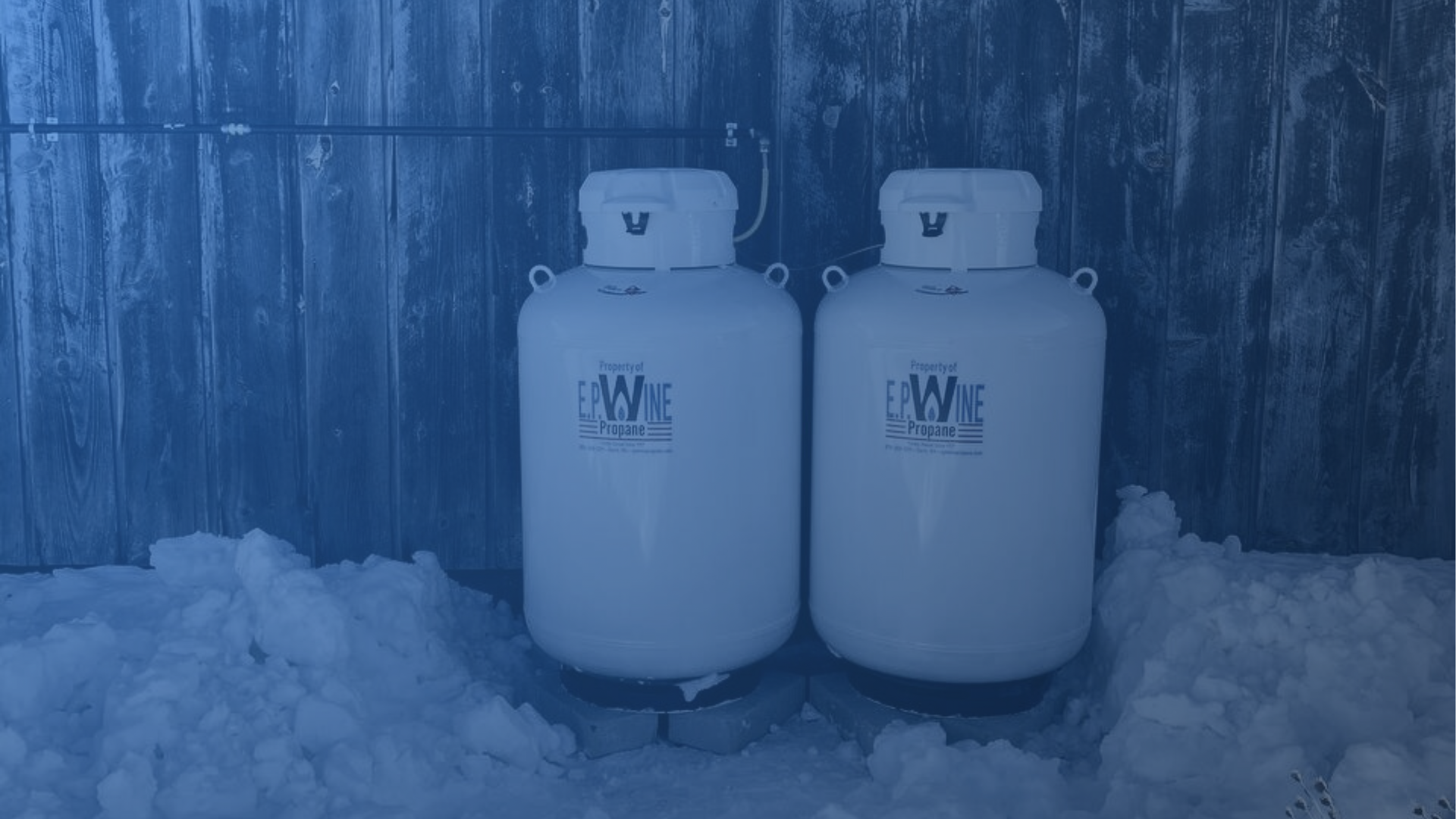 Three white propane tanks next to a building on a stone platform in an outdoor setting.