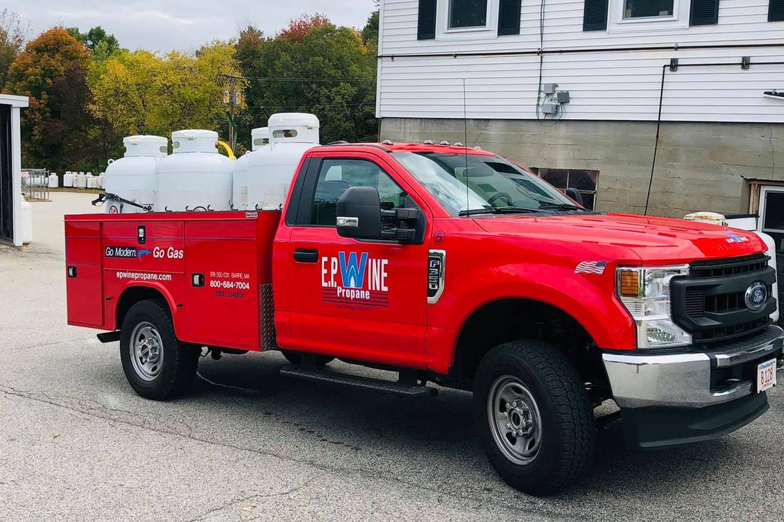 Red propane truck parked, loaded with tanks, in front of a building. 
