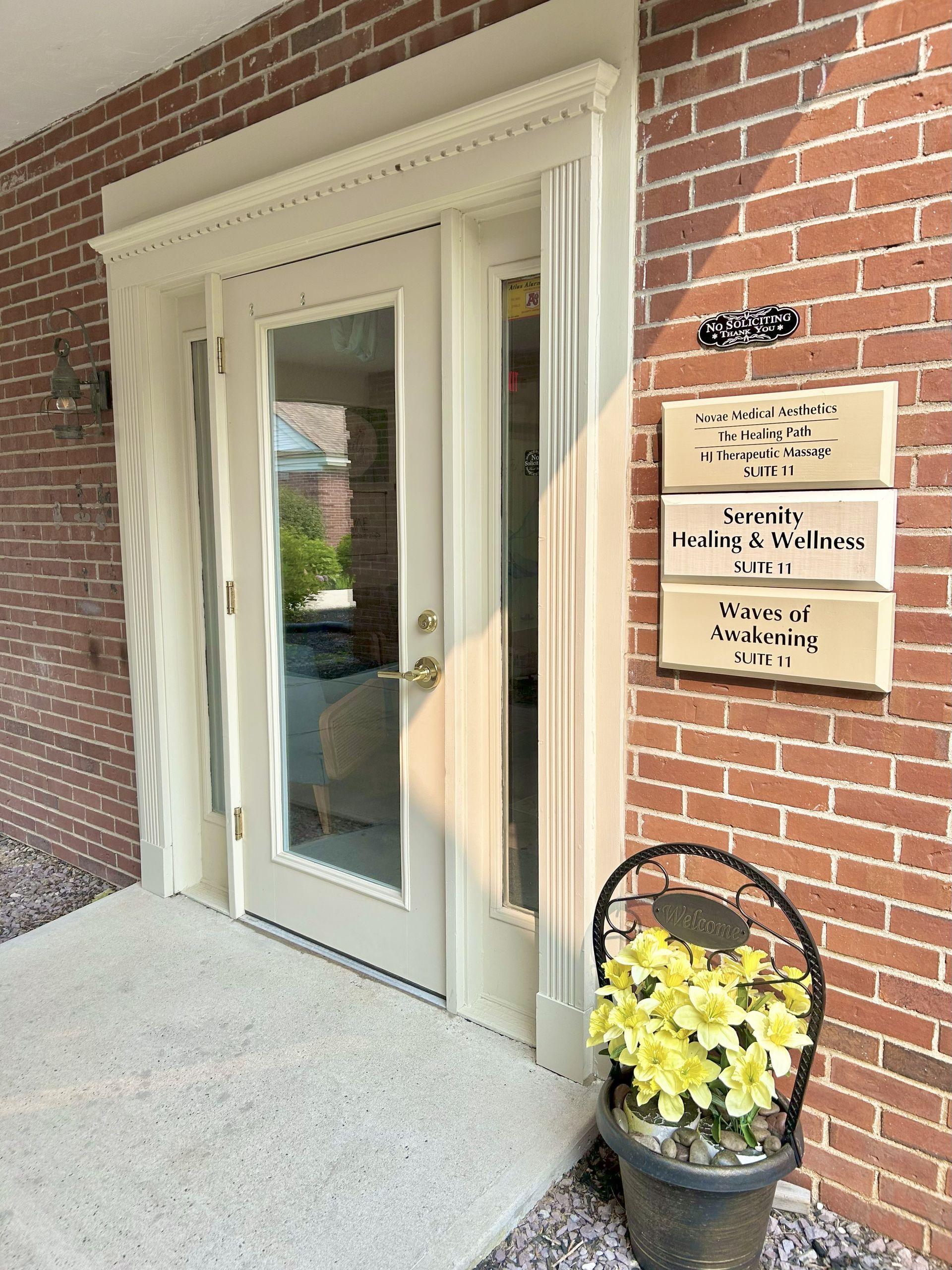 Exterior of brick building with glass doors and signage, a pot of flowers sits to the right.