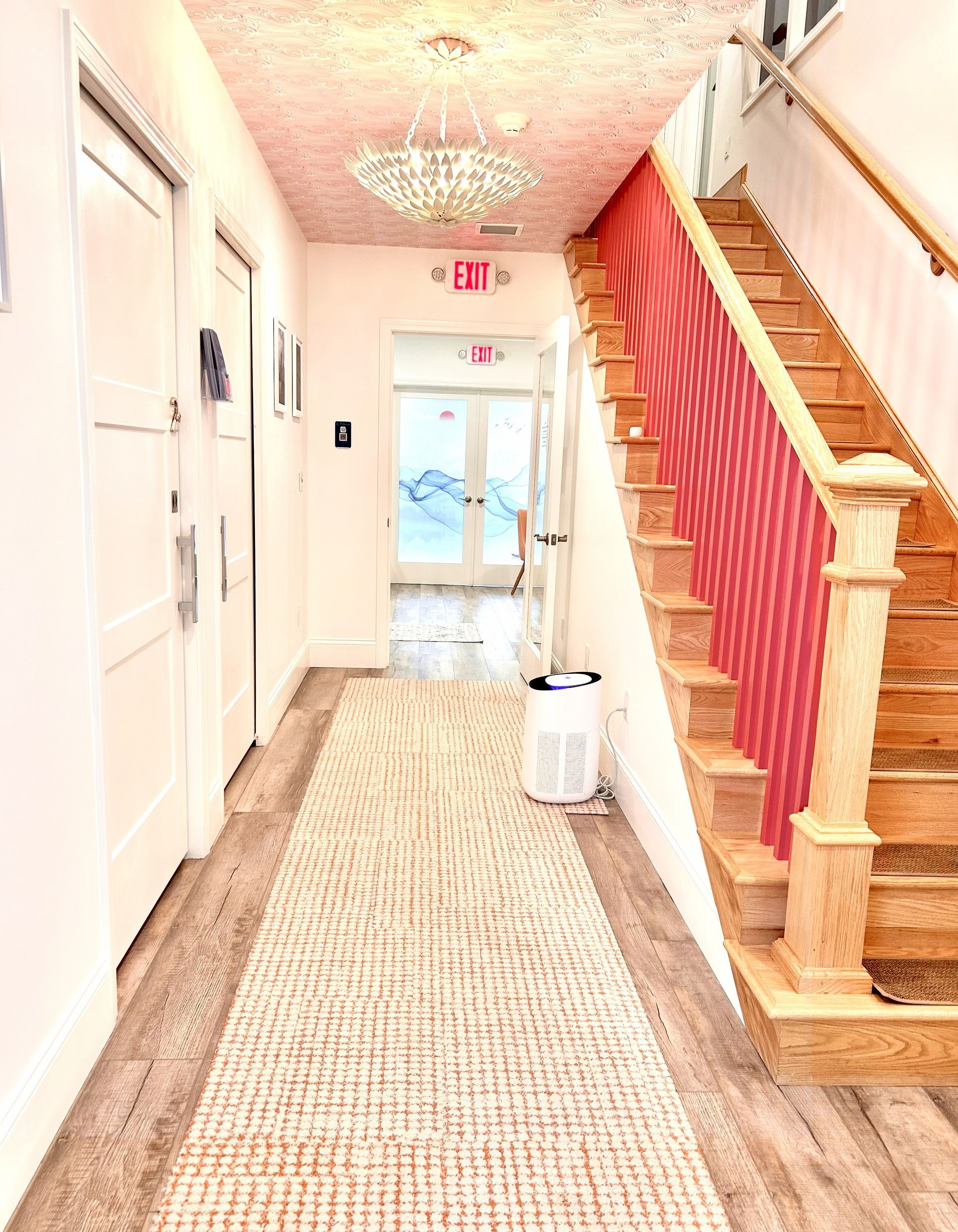 Hallway with stairs: white doors, patterned rug, red stair rail, and crystal chandelier.