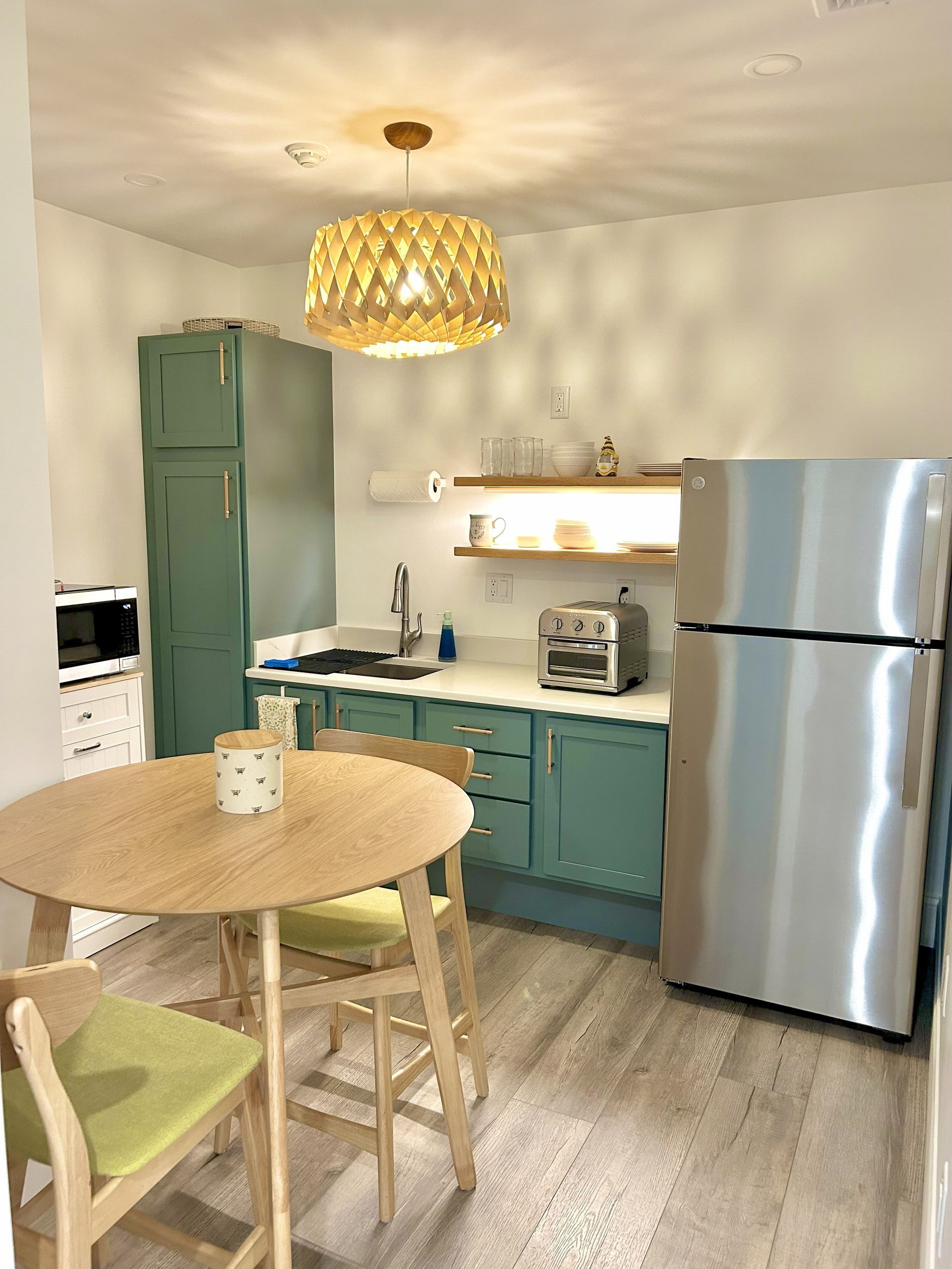 Small kitchen with a round table, green cabinets, and a stainless steel refrigerator.